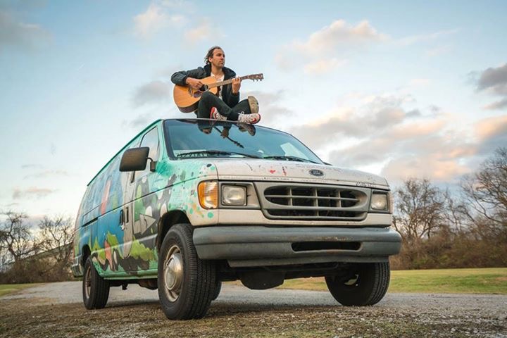 Noah Grove sitting on top of the graffiti Big Picture tour van with a guitar